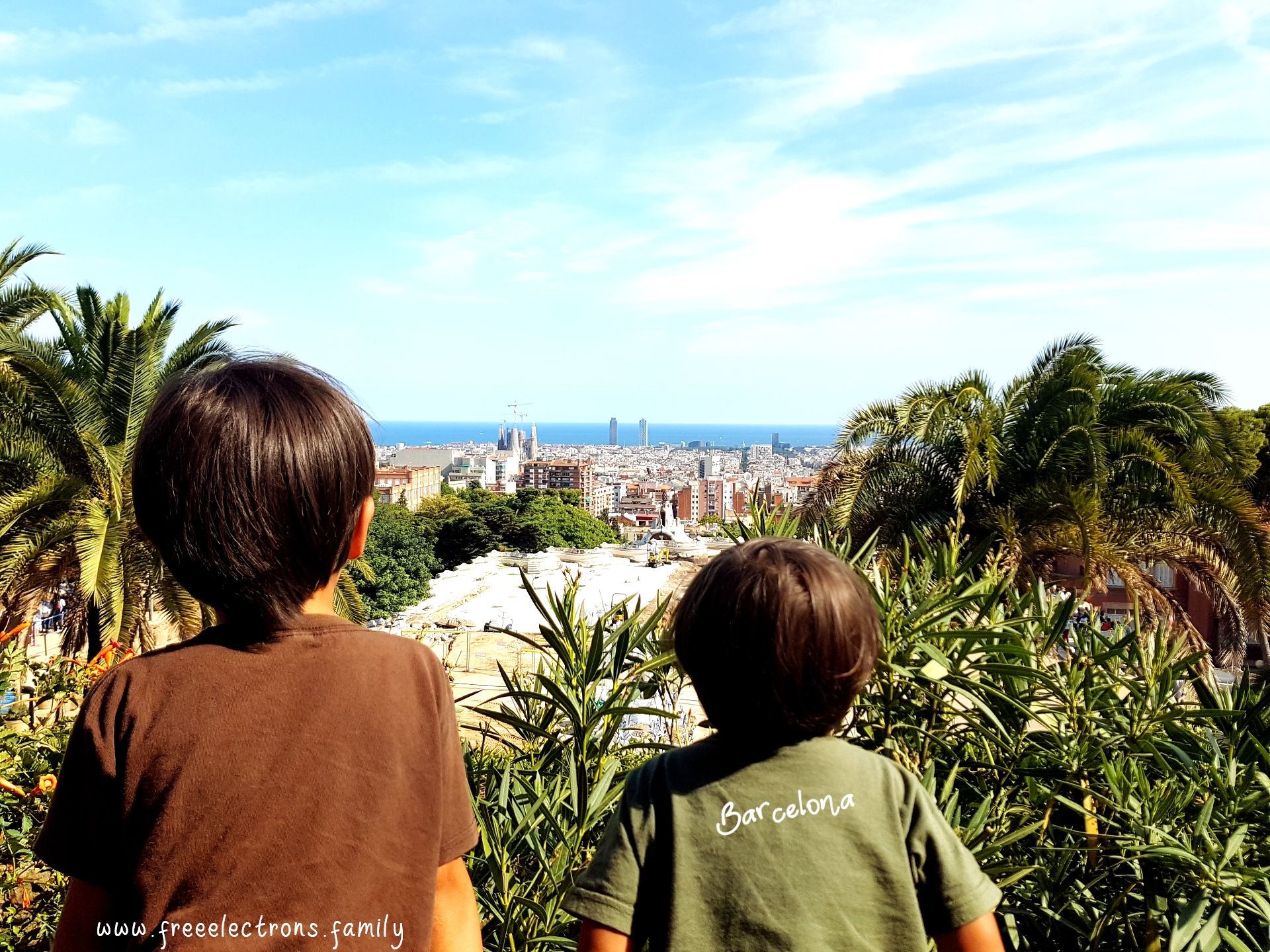 #FreeElectrons.Family - camping road trip Europe, Barcelona, Catalonia. 

Two young kids enjoying the view of Barcelona from a viewpoint near the Gaudi House Museum.

Text reads: Barcelona and www.freeelectrons.com.