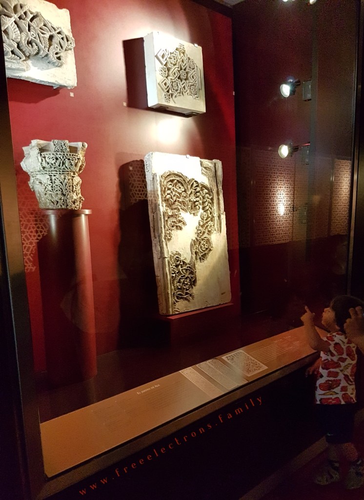 A toddler looking and pointing with apparent curiosity at the ancient decorative stone pieces at the Aljaferia. Third stop on our #FreeElectrons.Family summer camping road trip Europe, Day 5 in Zaragoza.