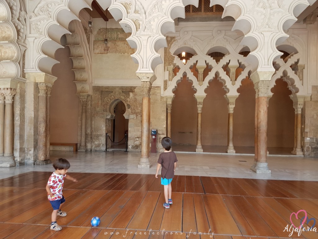 Two young children playing soccer in the the intricately decorated and beautifully renovated welcome hall of the Aljaferia. Text reads: www.freeelectrons.family and Aljaferia (with a drawing of 2 interlocking hearts behind it).
