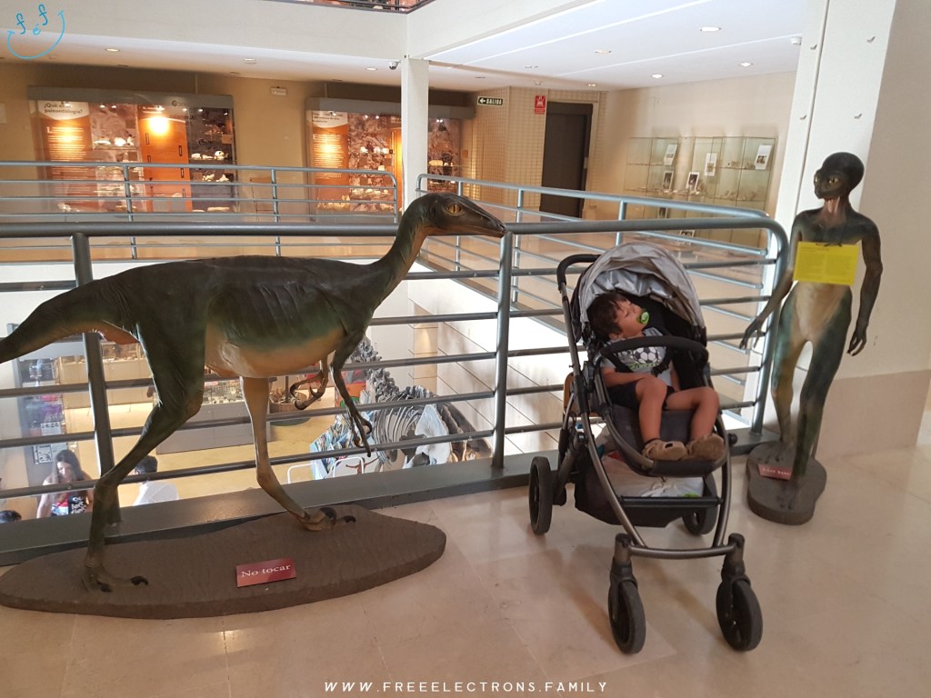 A child sleeps in a stroller/pram, fitting right in between an I-love-to-eat-little-kids-asaurus and a I-just-got-out-of-Roswell alien... at the National Museum of Natural History. #FreeElectrons.Family - camping road trip Europe, Madrid Science Museum alien dinosaur.