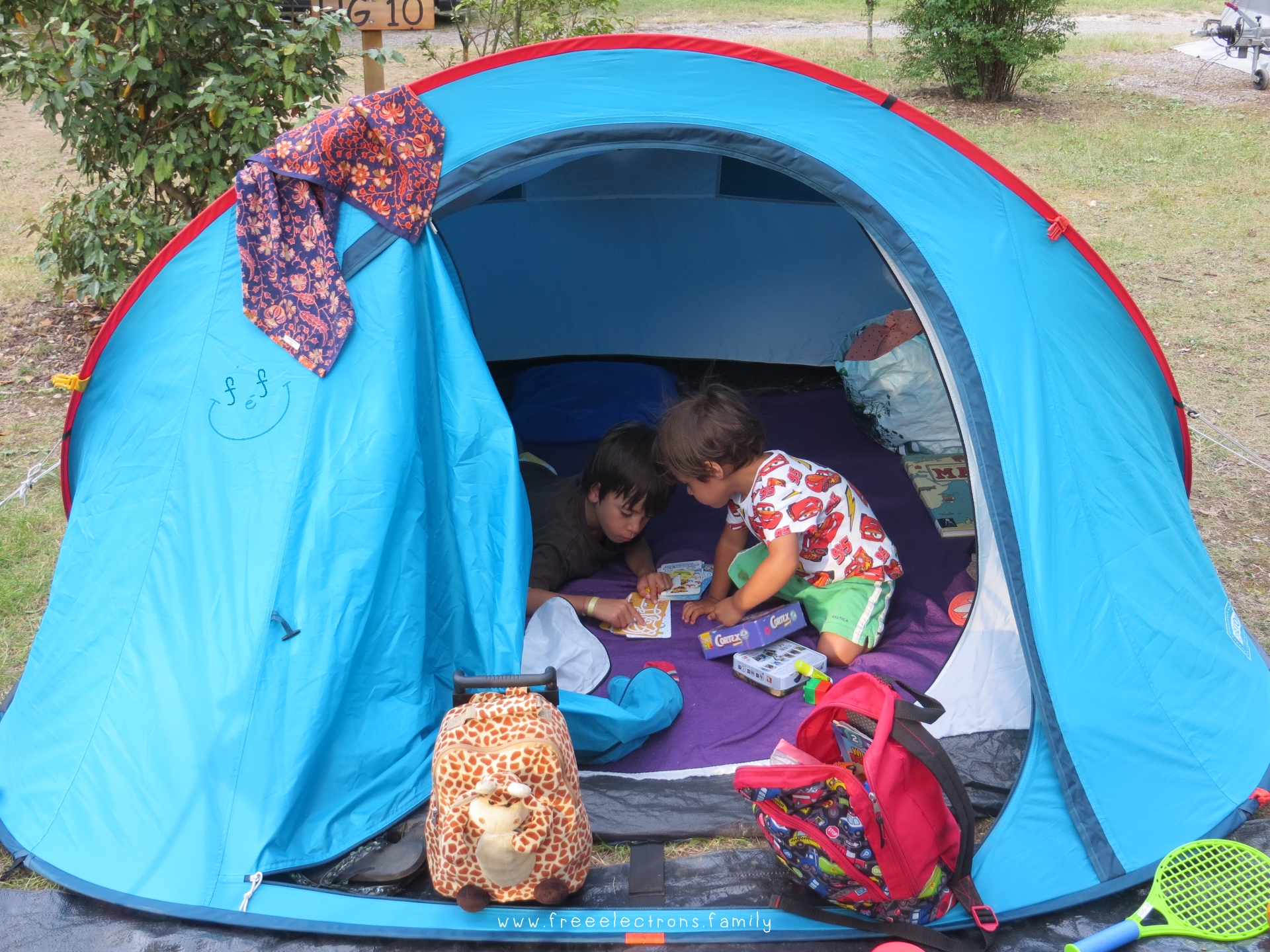Two young boys inside a camping tent, reading.  Text Reads: www.freeelectrons.family.

#FreeElectrons.Family - camping Europe, what to bring, tent.