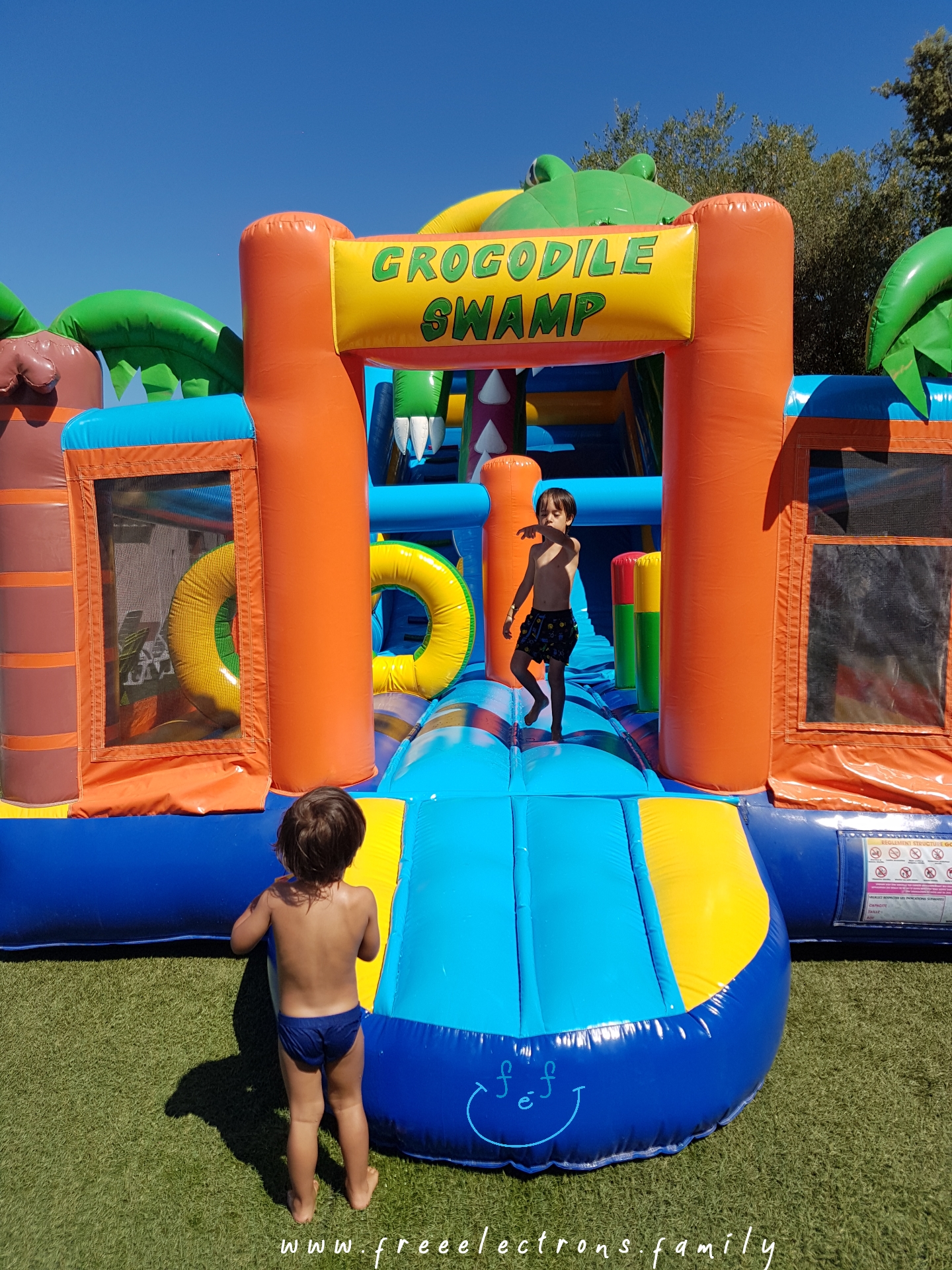 2 young boys in a huge "Crocodile Swamp" jump-and-slide,  inflatable play structure.

#FreeElectrons.Family - camping road trip Europe, Agde France.