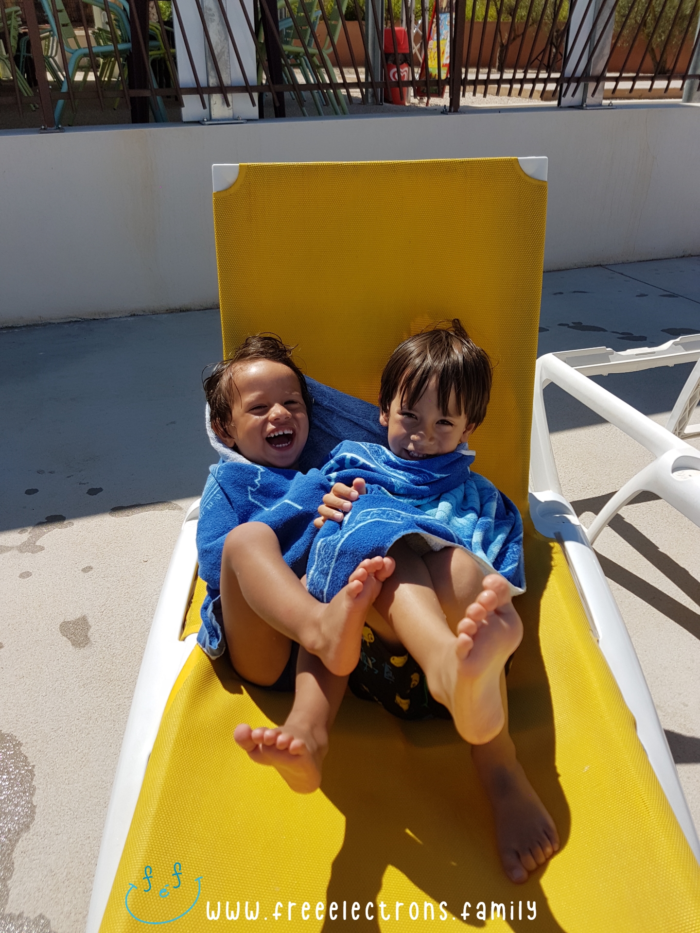 2 young boys wrapped in one towel, laughing to their hearts content, by the side of the pool.

#FreeElectrons.Family - camping road trip Europe, Agde France.