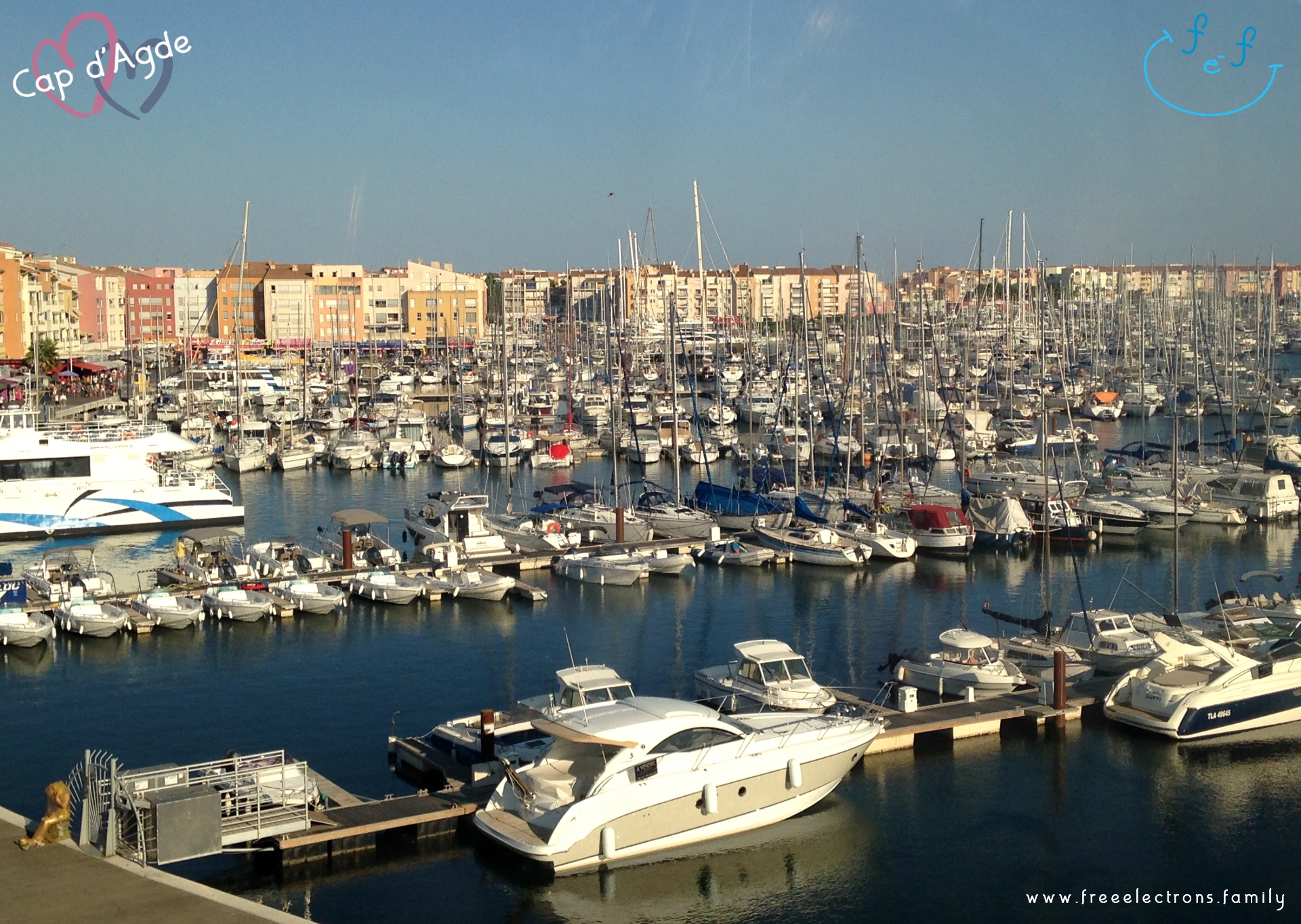 A view (from the ferris wheel) of Cap d'Agde's marina packed with modern boats in the foreground and buildings in the background.

#FreeElectrons.Family - camping road trip Europe, Cap d'Agde France.