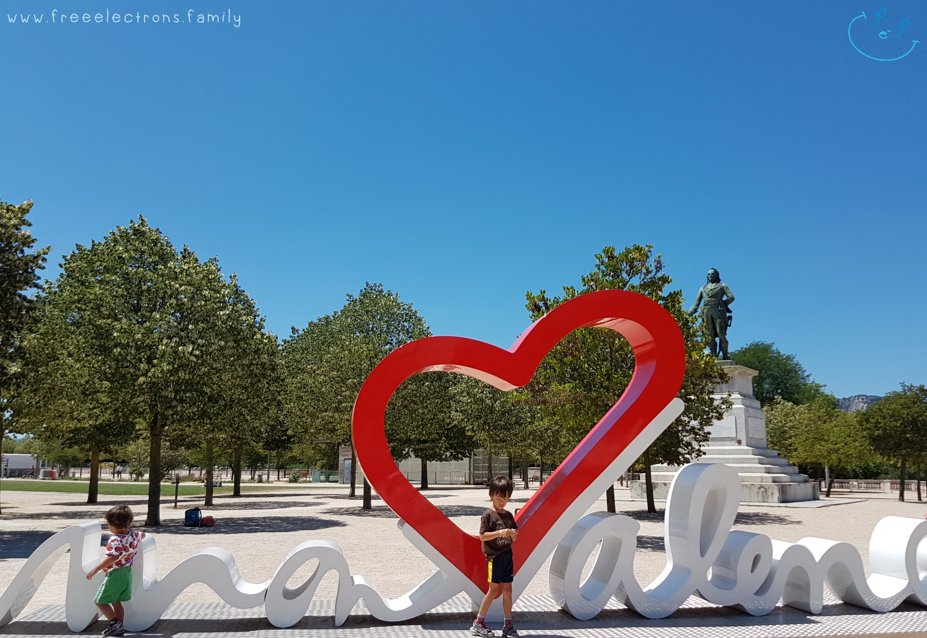 Two young boys at the "heart" of Valence with a monument and trees in the background. 

#FreeElectrons.Family - camping road trip Europe, Valence.