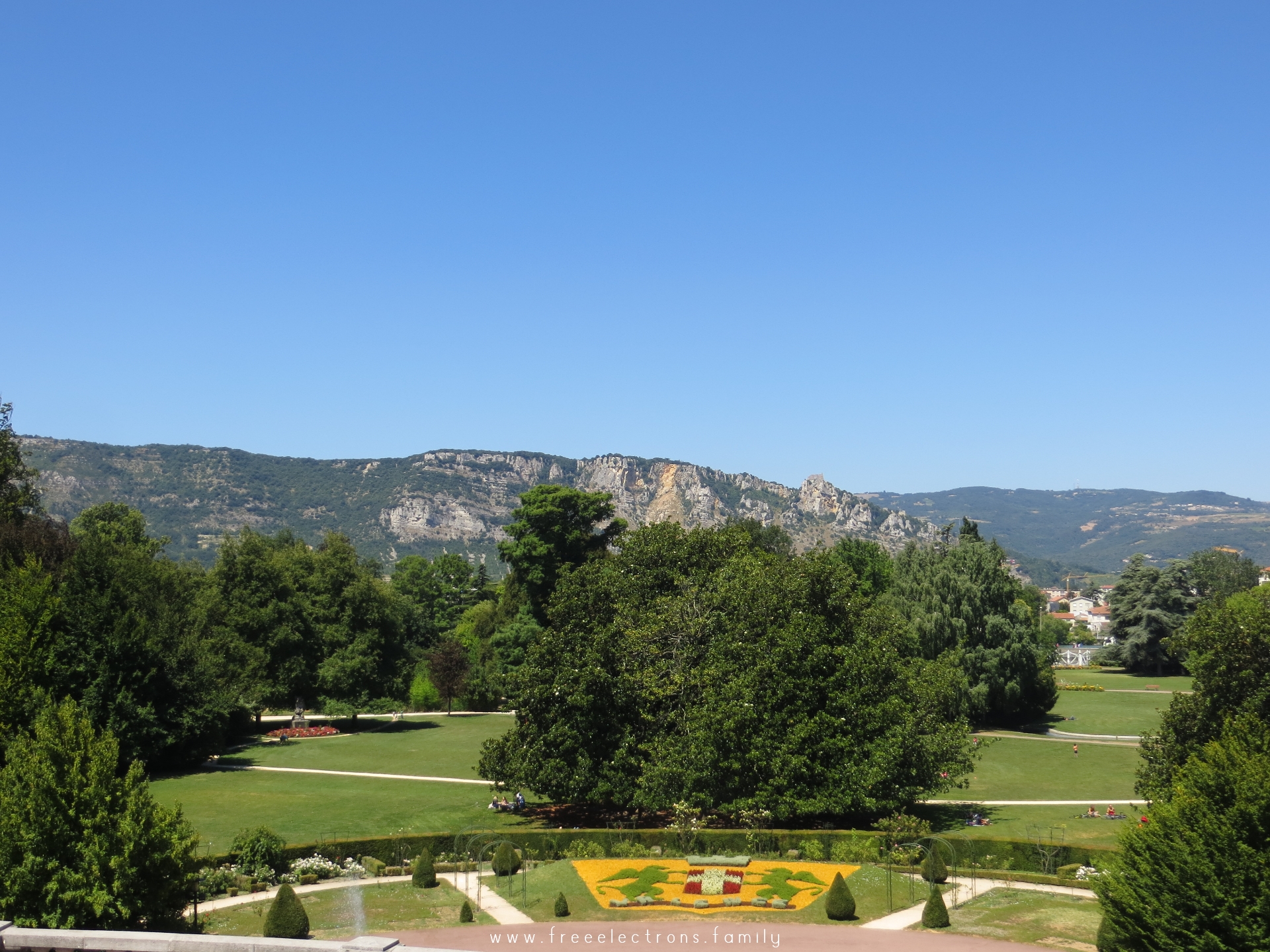 Entrance to Parc Jouvet with a view of the rocky slopes of a nearby mountain, under clear blue summer sky.

#FreeElectrons.Family - camping road trip Europe, Valence.