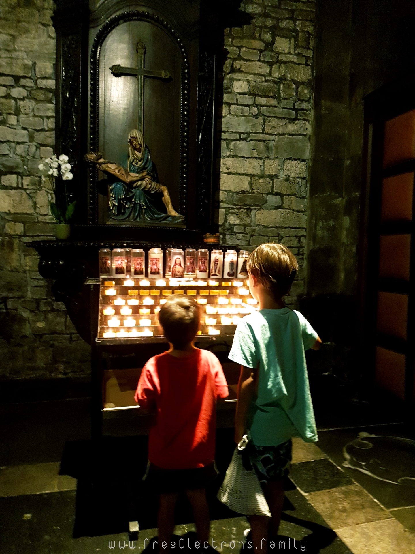 Two young children lighting candles at a chapel in the Basilica of Our Lady.  The altarpiece had an image of Mary carrying the dead body of Jesus.

#FreeElectrons.Family - camping road trip Europe Maastricht