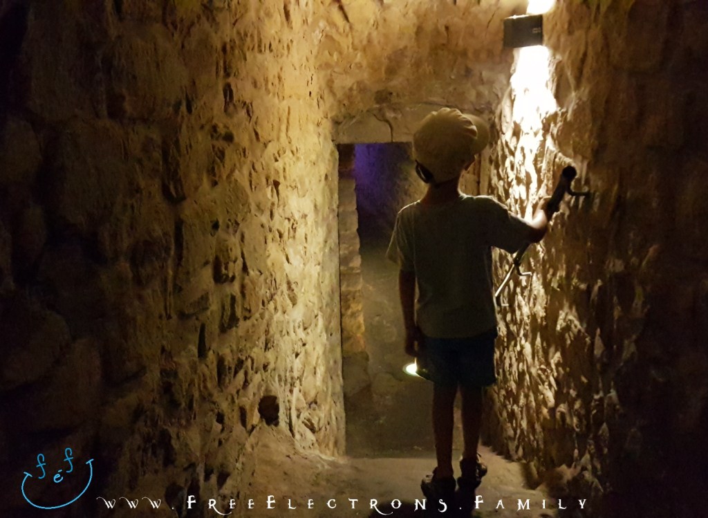 A young boy, back-turned, explores a lighted tunnel into the depths of the underground galleries of Casemates du Bock.

Text on picture reads: www.FreeElectrons.Family with an inserted smiley face (custom icon) at a bottom corner. 