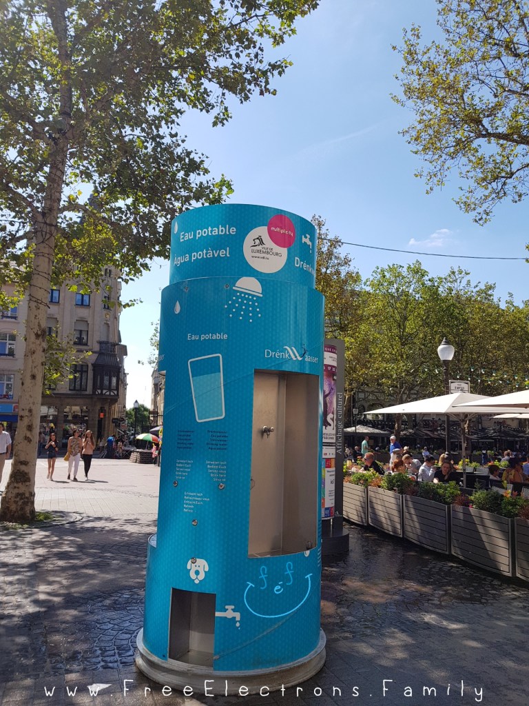A FREE light-blue-colored water station for people and dogs in a pedestrian city square in Luxembourg.

Text on picture reads: www.FreeElectrons.Family. 