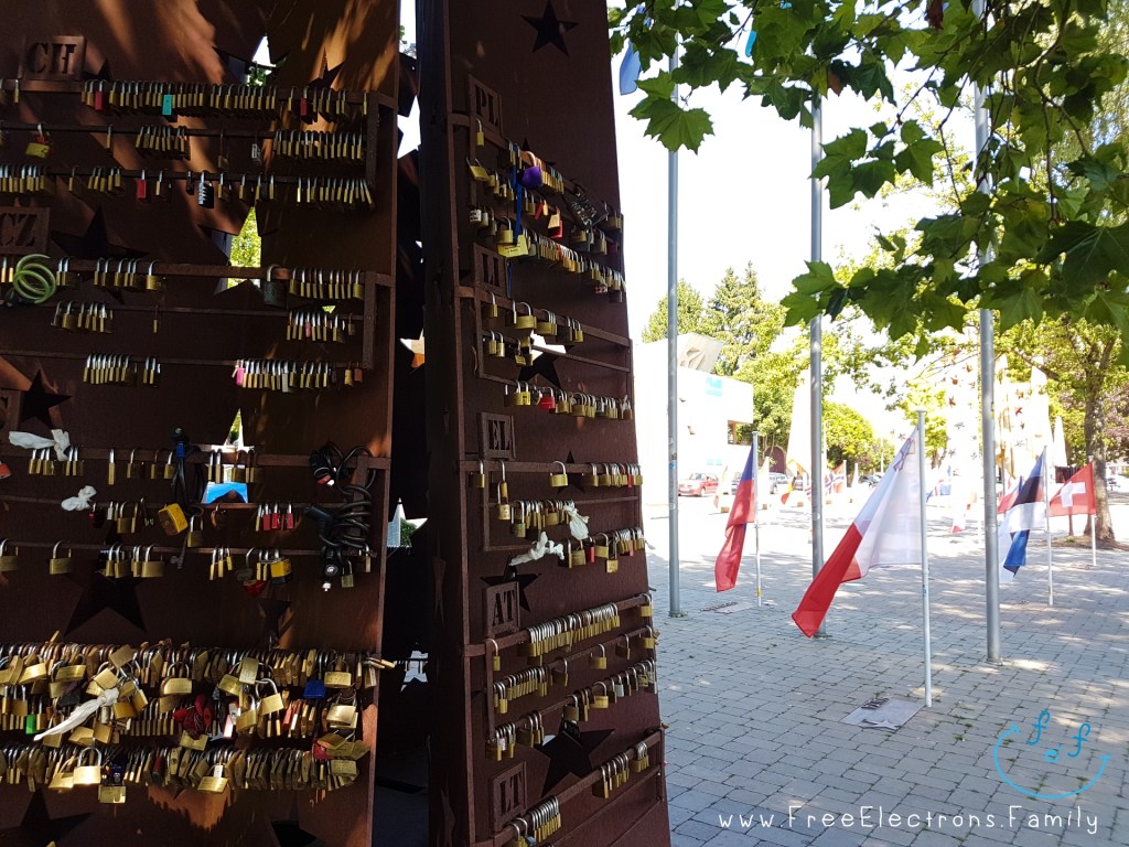 An iron monument with padlocks in a plaza with European flags.

www.FreeElectrons.Family