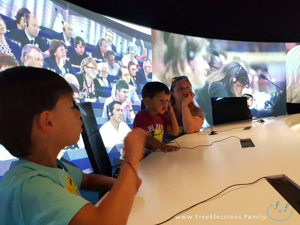 A mother and two young children engaged in the audio-visual presentation about the processes of the European Parliament.

Text on photo reads www.FreeElectrons.Family