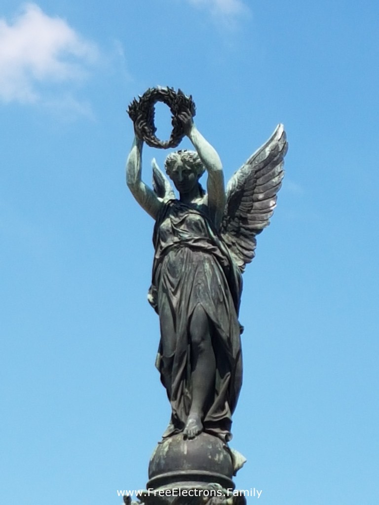 A close-up of Victory Monument (Siegesdenkmal) on a beautiful, blue-sky day.  

Text reads:
 www.FreeElectrons.Family