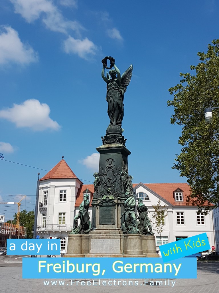 Victory Monument (Siegesdenkmal) on a beautiful, blue-sky day.  

Text reads: a day in Freiburg, Germany with Kids; www.FreeElectrons.Family