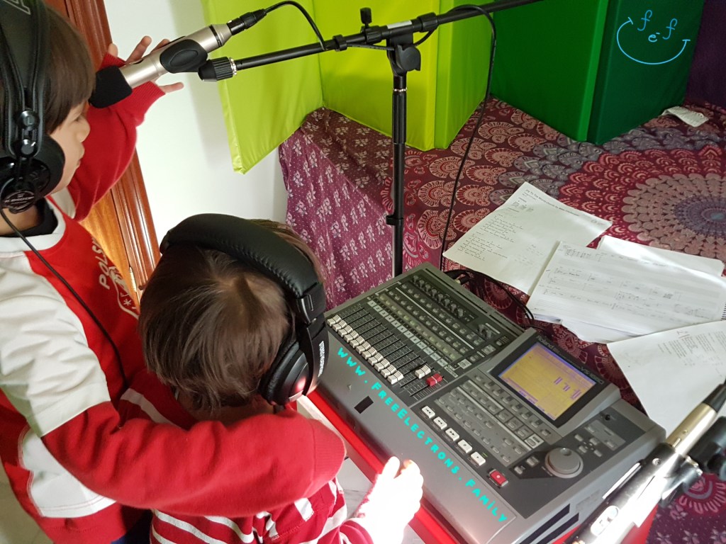 Two young boys with headphones and microphone in front of a mobile home recording "studio".

Text reads:  Joy to the World, Villancicos Mix, Rumba Flamenca Mix Spanish-English-Family Video.

www.FreeElectrons.Family