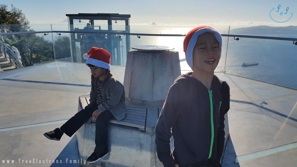 Two young boys with Christmas hats on, one laughing, on a high ground overlooking the Mediterranean sea with ships on it and a mountain range in the background.

www.FreeElectrons.Family