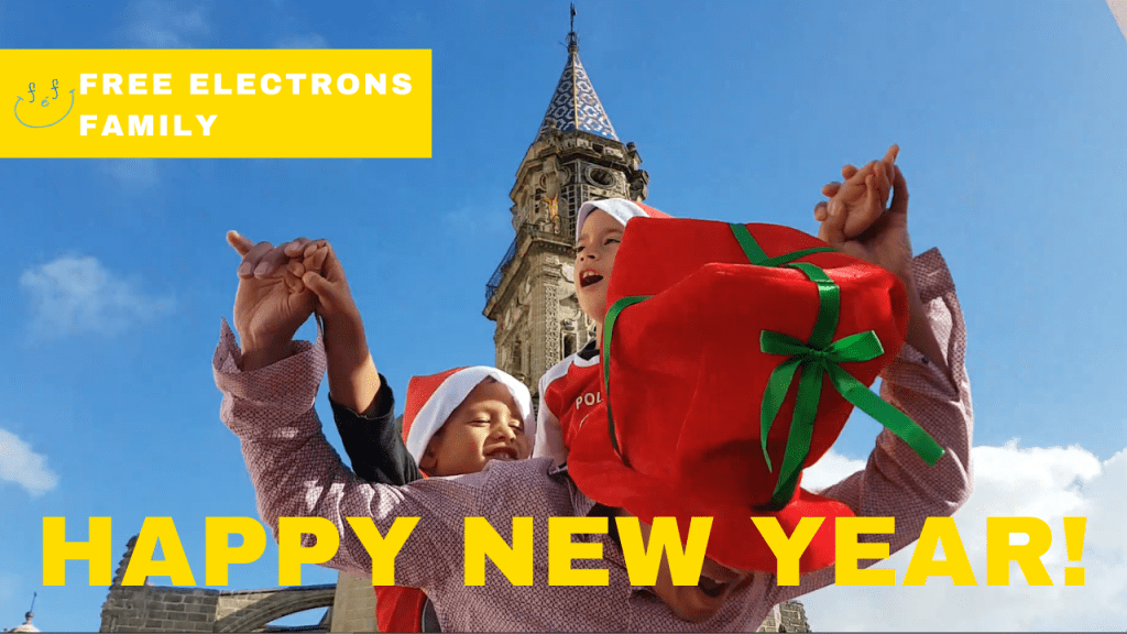 A father and his two young boys with Christmas hats on dancing with happy faces, with the bell tower of a church behind them.

Text reads: Happy New Year; Free Electrons Family