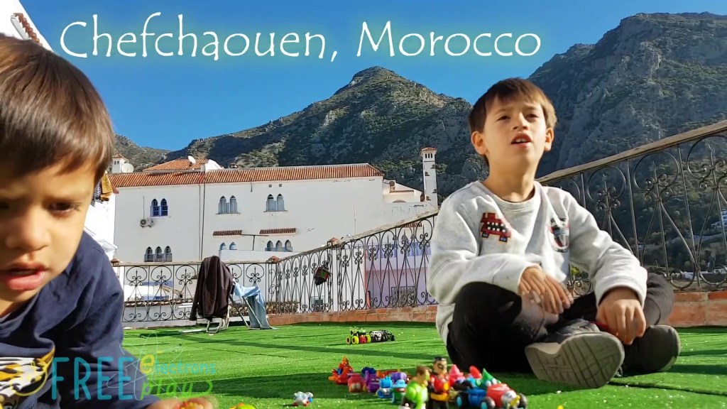 Two young boys with their toys on a balcony in Morocco with the Chefchaoeun mountain peaks behind them.
-Free Electrons Family