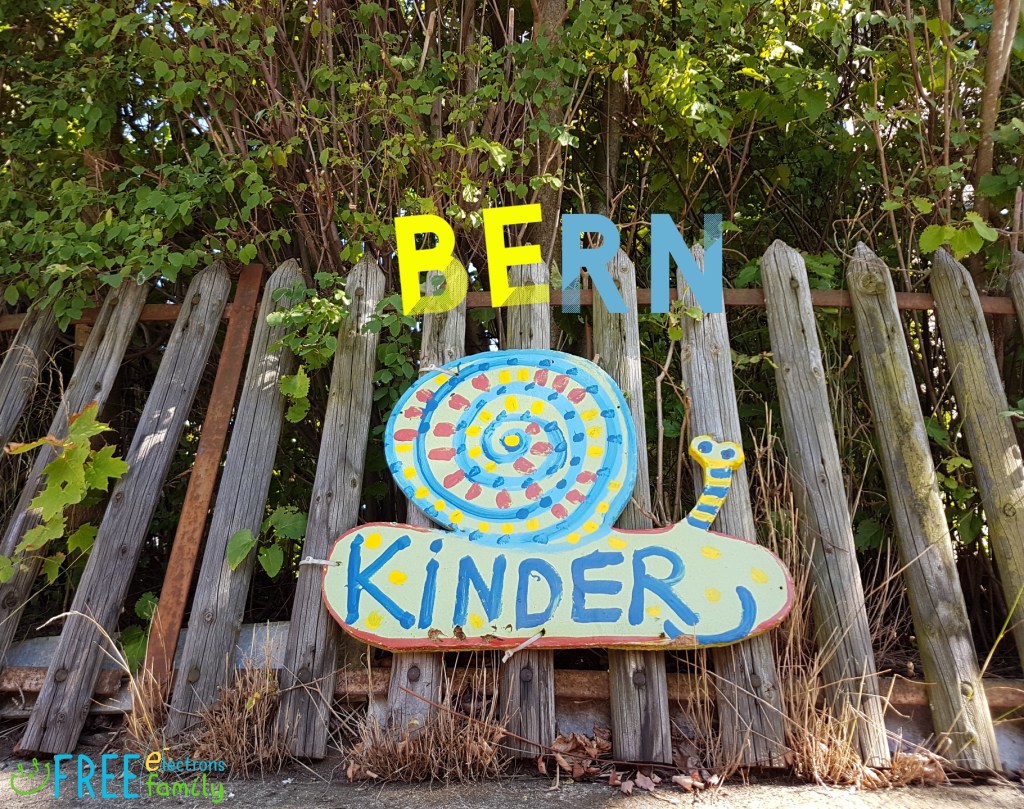 A rustic fence with overgrown vegetation and a made-up sign in a form of a snail that reads "Kinder", with "BERN" super-imposed in different colors to read "Be Kinder!"

www.FreeElectrons.Family 