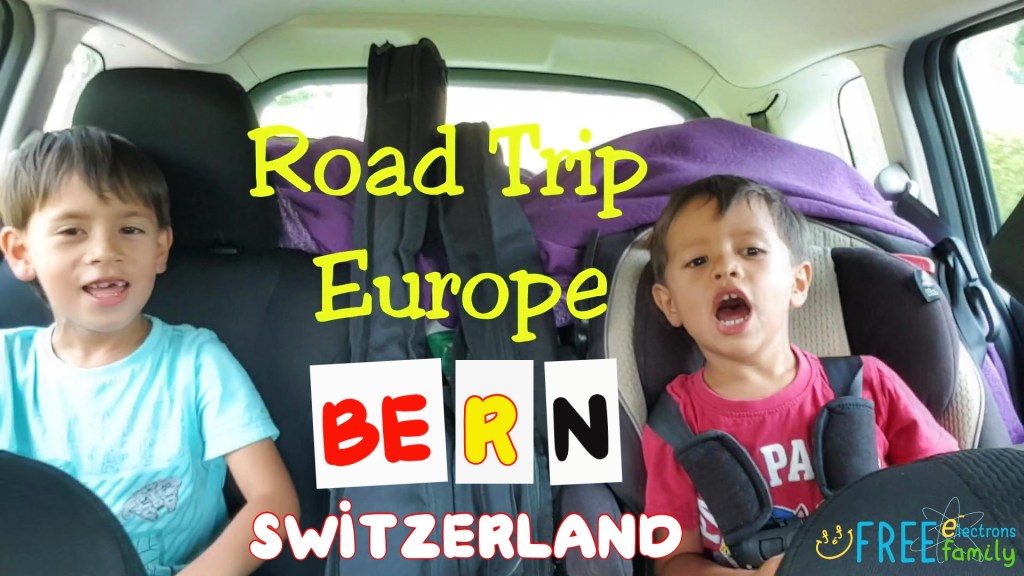 Two young children in a car, cheering, smiling.  Text reads: Road Trip Europe Bern, Switzerland.
www.FreeElectrons.Family 