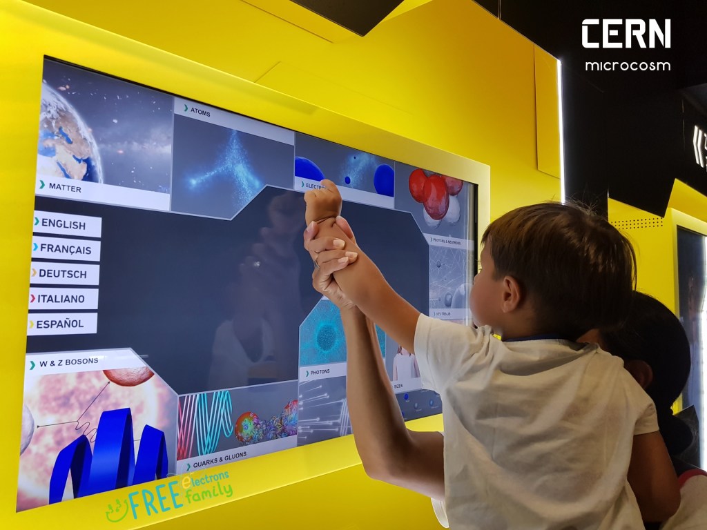 A young kid, carried by a parent, interacting with an informative touch screen in CERN's microcosm exhibit.
#FreeElectrons.Family