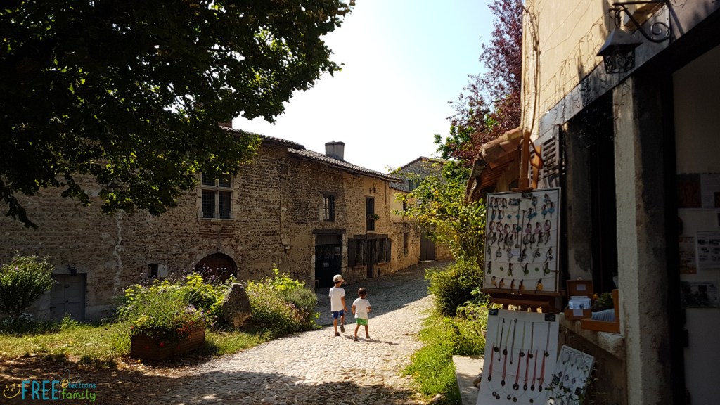 Two young boys in the middleground walking away, on their own, on a quiet cobblestone street, with various craftwerk for sale from a shop in the foreground, and other stone houses in the background.

www.FreeElectrons.Family