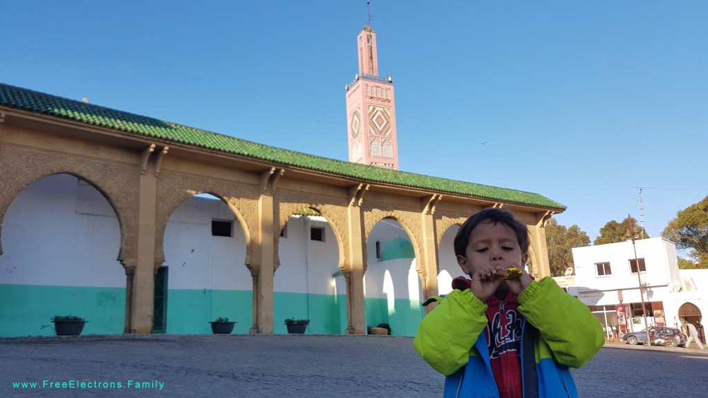 A young boy with a whistle in a market square with a mosque tower in the bacground.