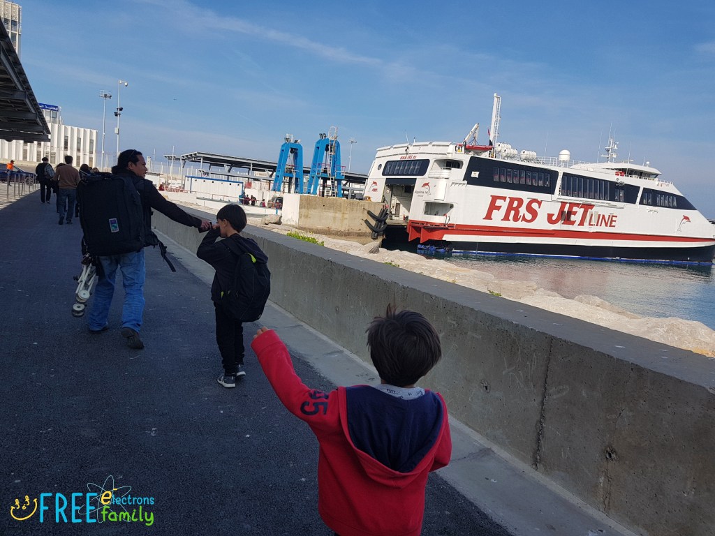 A father and two young boys  with backpacks heading towards a ferry.