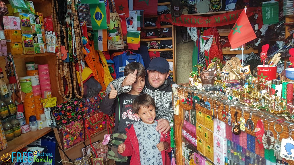 Two young boys and a shop owner of a souvenir shop smile and give a thumbs up for the camera.